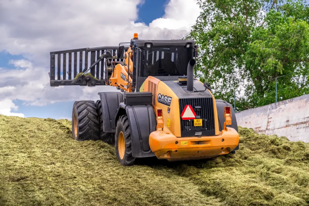 Traktor CASE s nakladačem na hromadě trávy.