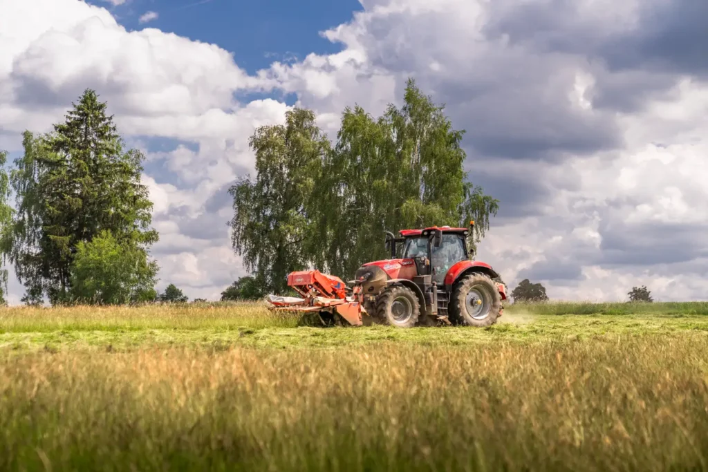 Traktor pracující na poli s modrou oblohou a mraky.