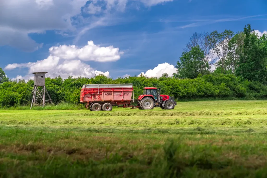 Traktor s vlečkou na louce pod modrou oblohou.