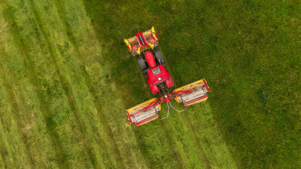 Červený traktor s žacími stroji na poli.